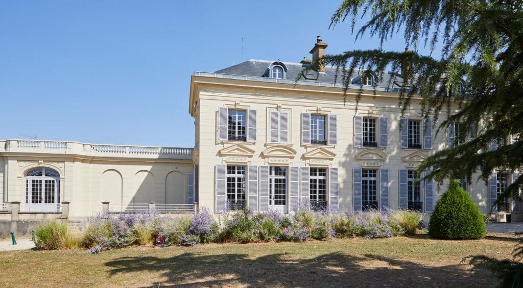 An exterior view of a three-story French country house featuring white wood windows and doors.